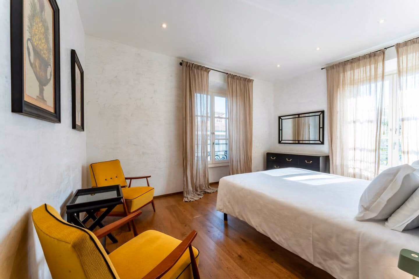 At Home — bright double bedroom with mustard mid-century armchairs and French doors to a juliet balcony