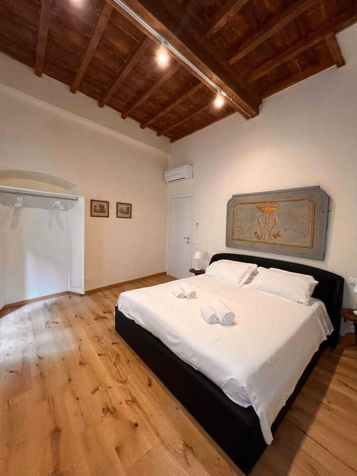 Sprone Left — master bedroom with an exposed timber-beam ceiling, wide oak floor and an antique painted headboard panel