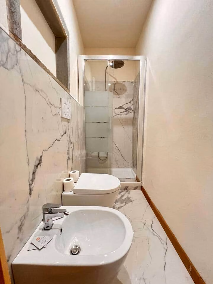 Sprone Left — bathroom clad in pale veined marble with a walk-in rain shower