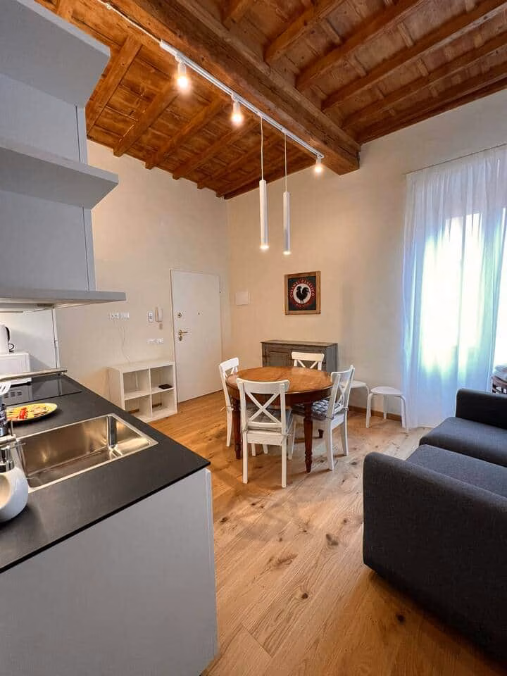 Sprone Right — open-plan living and dining area with an exposed timber-beam ceiling, oak floors, round table and grey sofa